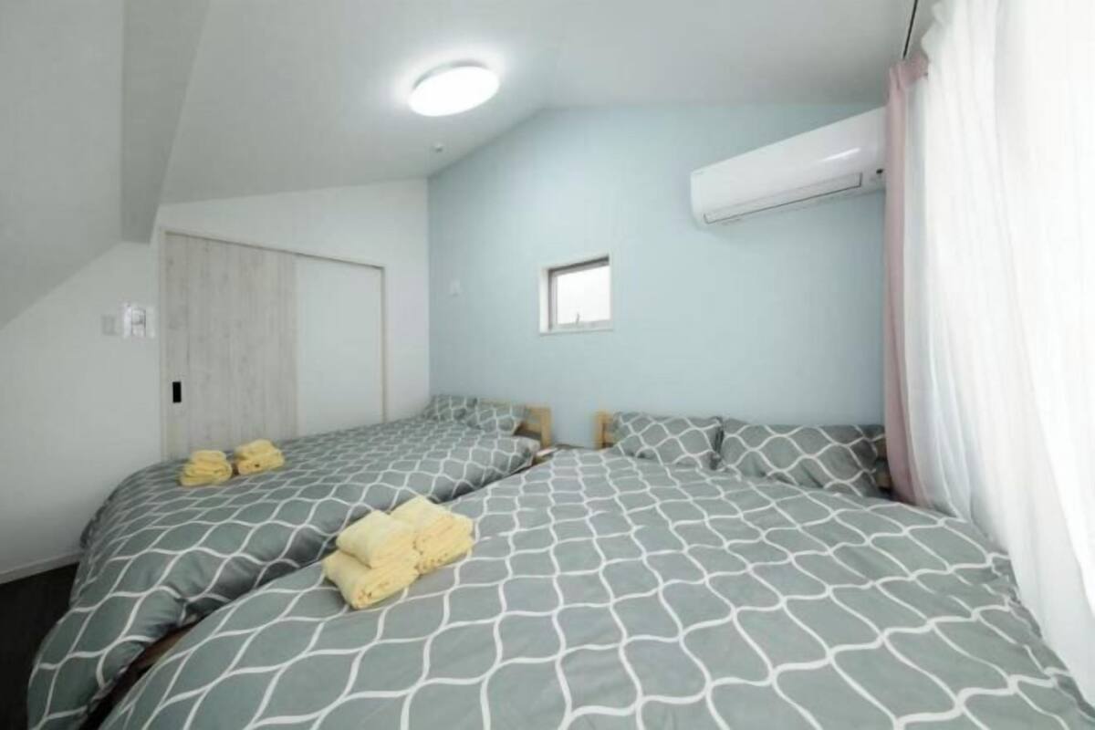A bedroom with two beds, a small window, and an air conditioning unit.