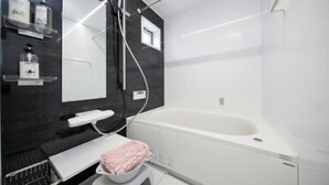A modern bathroom with a large bathtub, a mirror, and a shelf with toiletries. - Higashi Rokugou Black by Tranova (Tokyo)