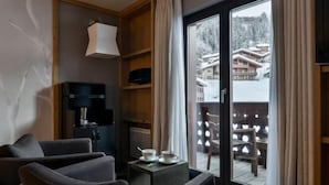 A hotel room with a sofa, a small table with cups, a lamp, a TV, and a sliding glass door leading to a snowy outdoor area. - Club Med Valmorel (Les Avanchers-Valmorel)