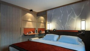 A hotel room with a bed, a nightstand, a wall-mounted lamp, and a shelf with a telephone and other items. - Club Med Valmorel (Les Avanchers-Valmorel)