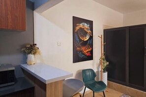A modern kitchen with a microwave, a white countertop, a green chair, and a wall-mounted painting. - MH Blueberry suite (Accra)