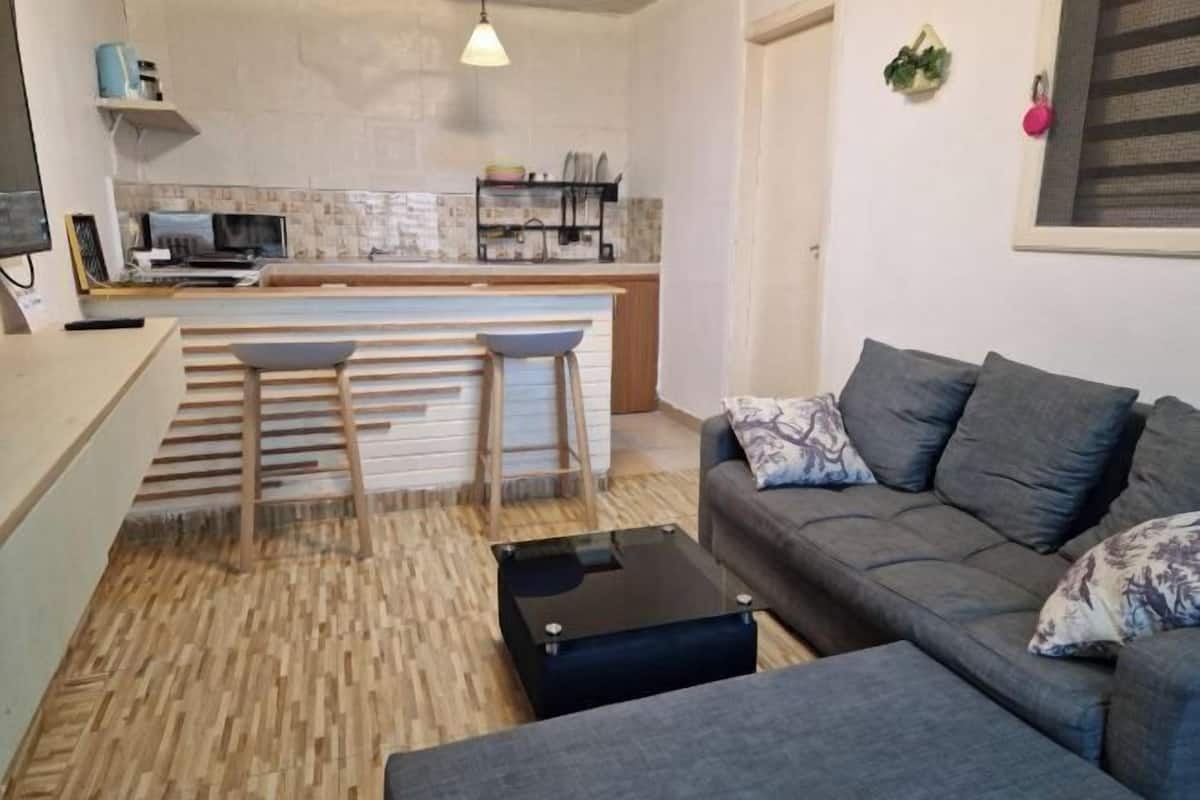 A compact living space with a kitchenette, a grey sofa, a coffee table, and a wooden floor.