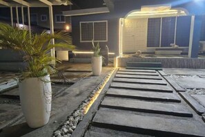Un sendero que lleva a una casa con porche, plantas en macetas y una entrada bien iluminada.