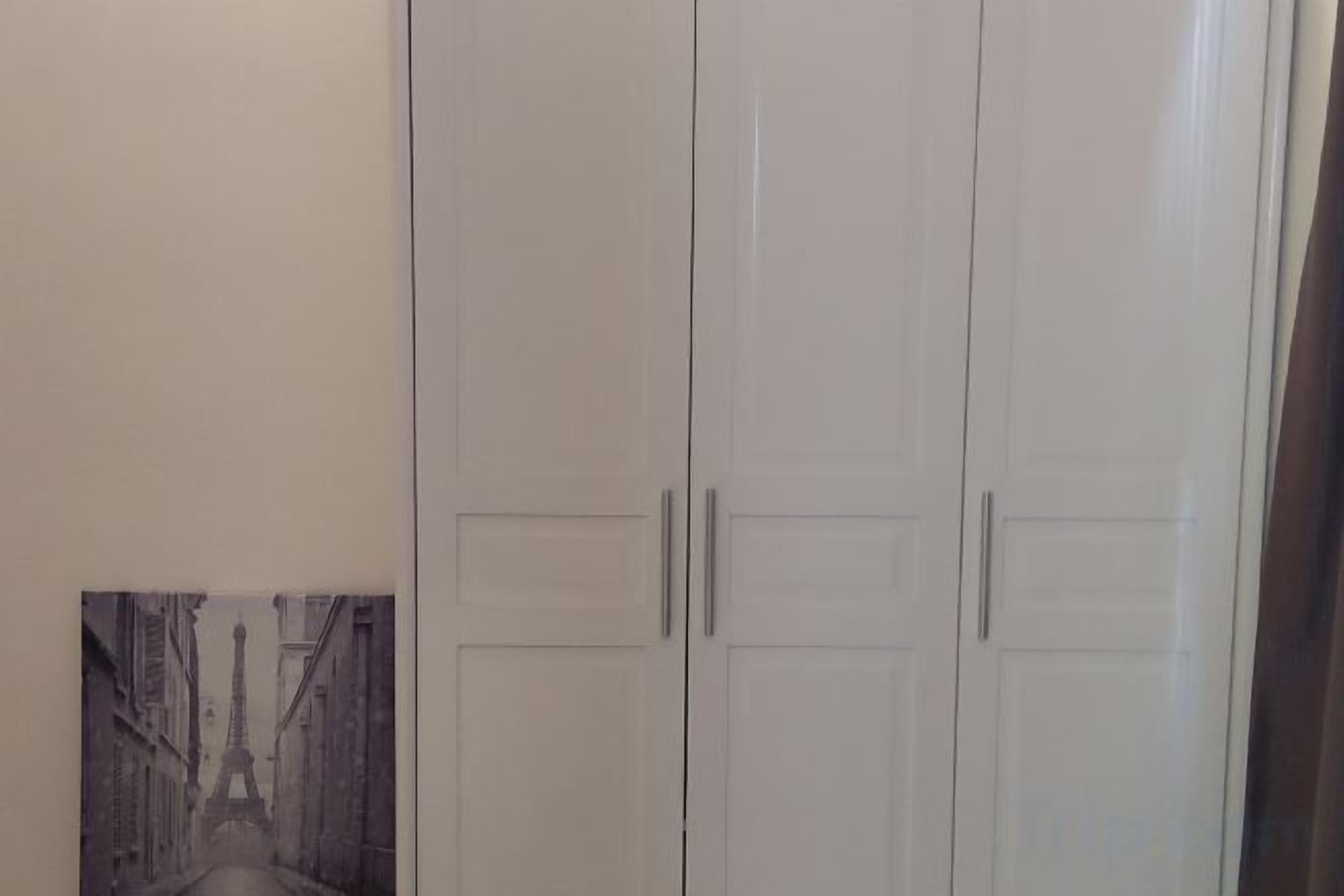 Guarda-roupa branco fechado com duas portas e um pequeno quadro emoldurado mostrando uma cena de rua.