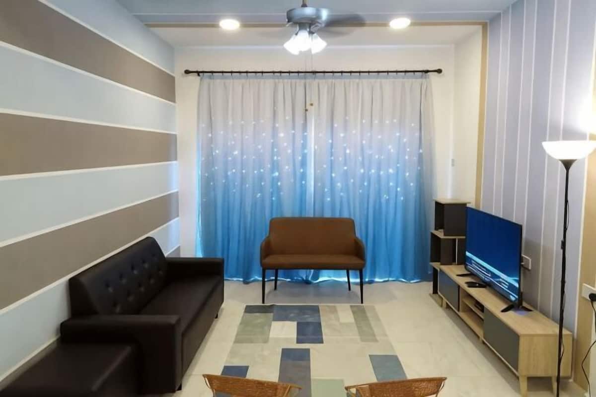 A living room with a sofa, a television, a floor lamp, and a patterned rug.