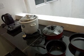 Une cuisine équipée d’un cuiseur à riz, d’une bouilloire et de deux casseroles, le tout posé sur un plan de travail noir.