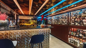 A bar area with a geometric patterned wall, a bar counter, and shelves of liquor bottles. - DAY & NIGHT by THE MOMENT (Chiang Mai)