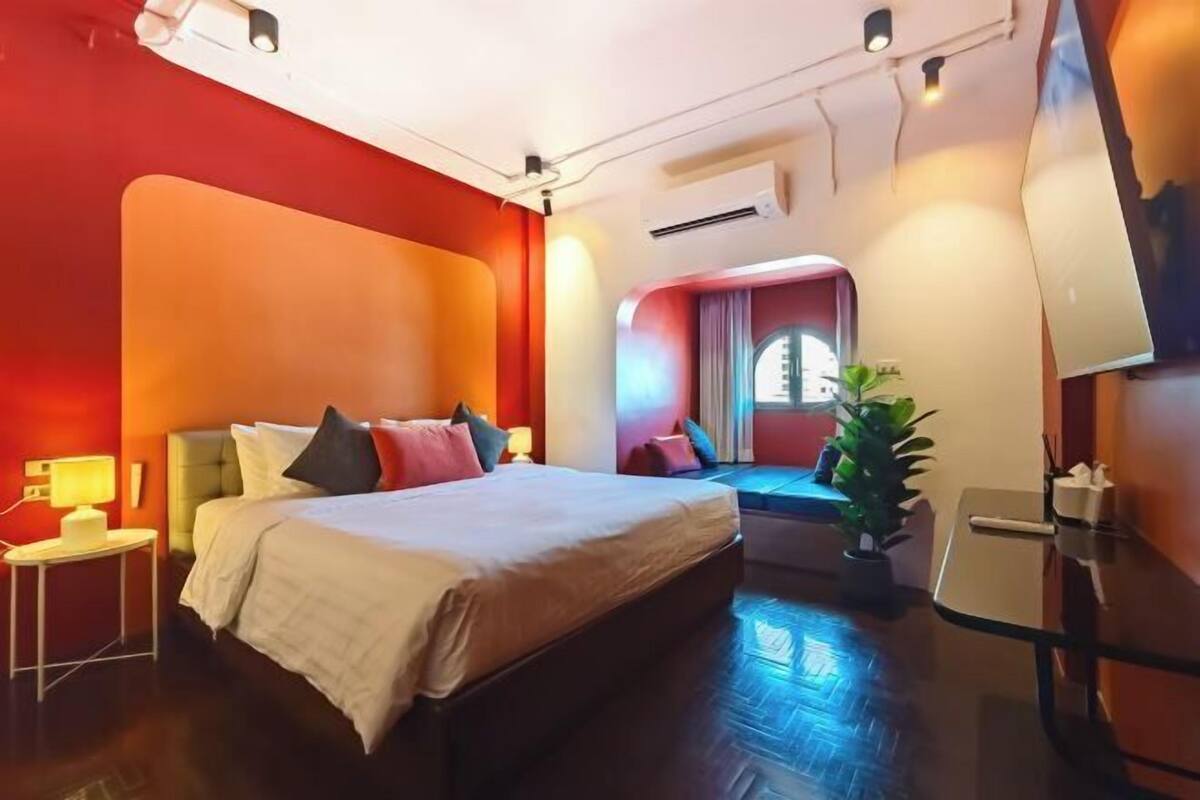 A hotel room with a large bed, bedside tables, a potted plant, and a window with curtains.