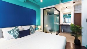 A modern hotel room with a bed, a nightstand, a lamp, a potted plant, and a bathroom visible through a glass door. - DAY & NIGHT by THE MOMENT (Chiang Mai)