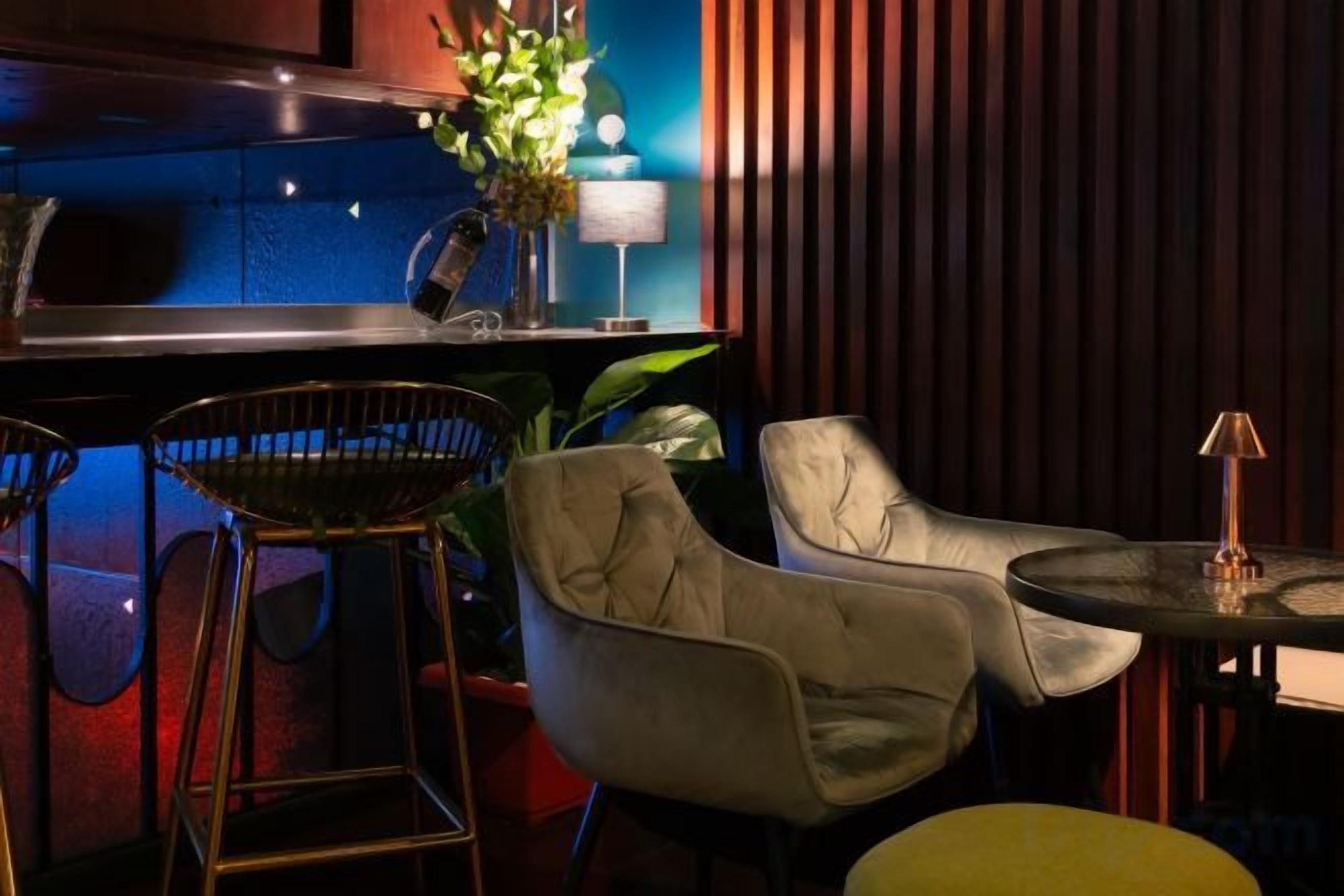 A bar area with stools, a bar counter, and a table with a lamp.