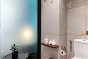 Un baño con inodoro, un estante con artículos de aseo personal y una planta en maceta.