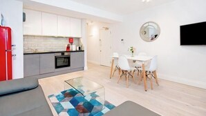 Une cuisine moderne avec des meubles blancs, un réfrigérateur rouge et un coin repas comprenant une table et des chaises blanches.