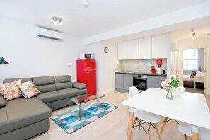 Un apartamento moderno con un sofá gris, un refrigerador rojo, una mesa de comedor blanca y una zona de cocina.
