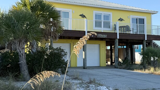 A yellow house with a balcony, a garage, and a palm tree in the yard. - Seaside Bungalow 1 Bedroom Home (Navarre)