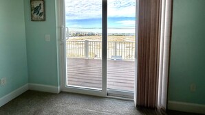 A room with a sliding glass door leading to a balcony with a view of a beach and houses. - Seaside Bungalow 1 Bedroom Home (Navarre)