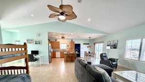 A spacious living area with a sofa, a dining table, and a kitchen in the background. - Seaside Bungalow 1 Bedroom Home (Navarre)