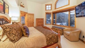 A bedroom with a large bed, a wooden headboard, a bench, a window with a view of trees, and a television on the wall. - 24 Autumn Brook 4 Bedroom Townhouse (Keystone)