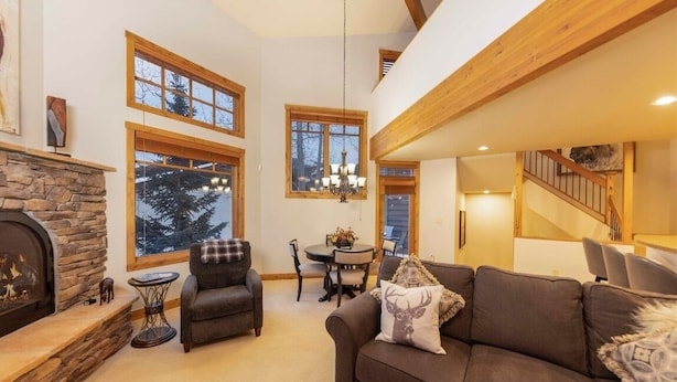 A cozy living room with a fireplace, a sofa, a dining table with chairs, and large windows. - 24 Autumn Brook 4 Bedroom Townhouse (Keystone)