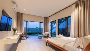 A modern hotel room with a large bed, a desk, and a chair. There are large windows offering a view of the outdoors. - THE GREEN LOTUS SAMUI (Koh Samui)