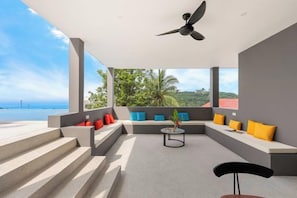 A modern outdoor seating area with steps leading to a terrace, a ceiling fan, and a view of the sea. - THE GREEN LOTUS SAMUI (Koh Samui)