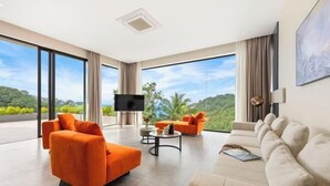 A spacious living room with a large window offering a view of greenery and hills. There is a flat-screen TV mounted on the wall and a coffee table with decorative items. - THE GREEN LOTUS SAMUI (Koh Samui)