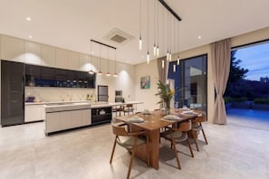 A modern kitchen with a central island, dining area with wooden chairs, and a large sliding glass door to a patio. - THE GREEN LOTUS SAMUI (Koh Samui)