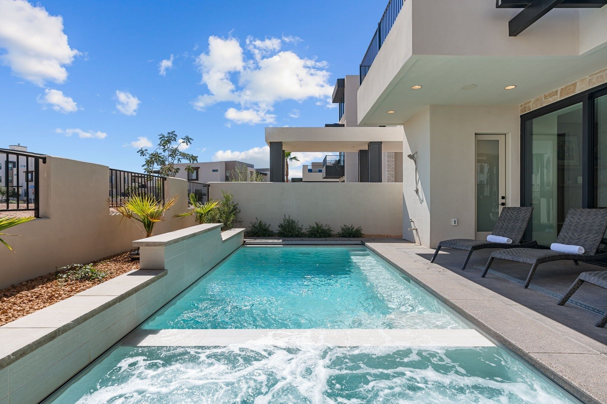 A modern outdoor pool area with a clear blue pool, a seating area with lounge chairs, and a contemporary building with large windows.
