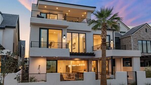 A modern two-story house with a balcony, large windows, and a well-lit interior.