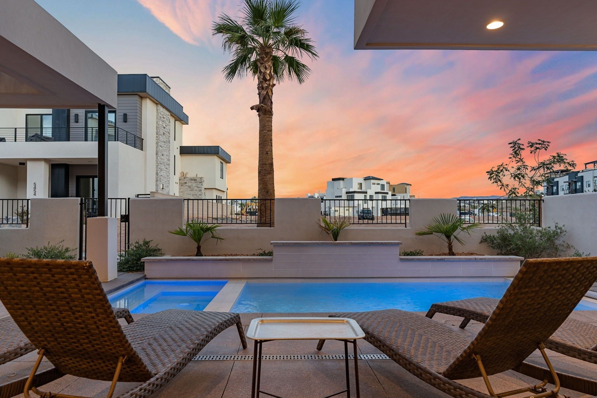 A poolside area with lounge chairs and a palm tree, overlooking a modern building complex.