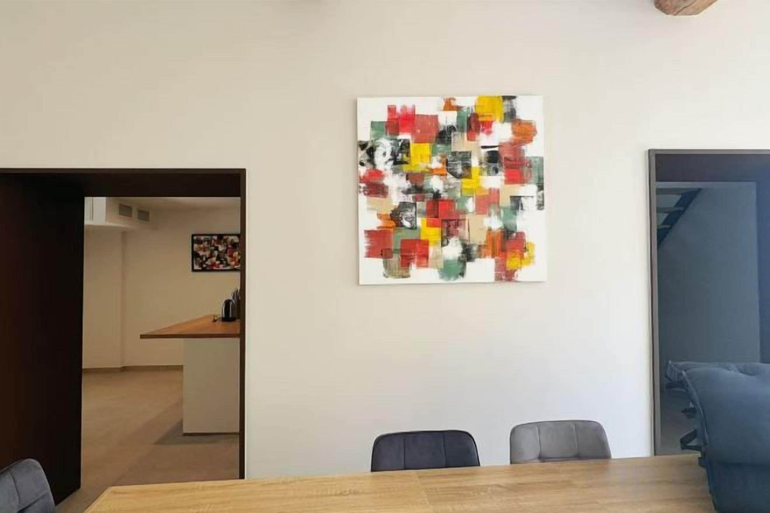 Ein Essbereich mit einem Holztisch und Stühlen, einem farbenfrohen abstrakten Gemälde an der Wand und Blick in die Küche.