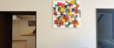 Ein Essbereich mit einem Holztisch und Stühlen, einem farbenfrohen abstrakten Gemälde an der Wand und Blick in die Küche.