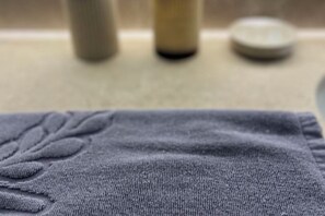 Detailaufnahme eines strukturierten Stoffes mit einem Blattmuster, möglicherweise ein Handtuch oder eine Decke, in einem Badezimmer.