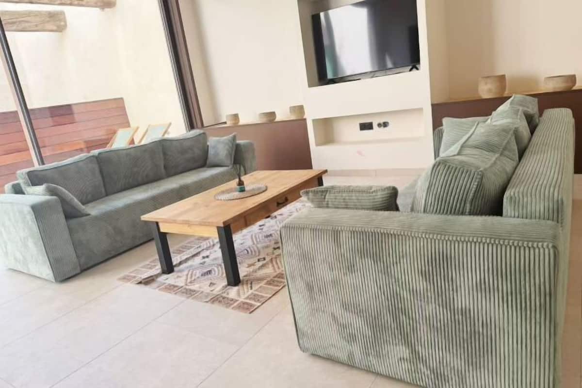 Ein modernes Wohnzimmer mit grauem Sofa, einem Holztisch und einem an der Wand befestigten Fernseher.