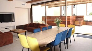 Een moderne woonkamer met een houten eettafel, blauwe en gele stoelen, een bank en een televisie.