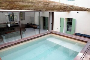 Une piscine dotée d’une enceinte en verre, d’une terrasse en bois et d’un espace détente avec un banc.