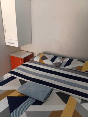 Un dormitorio con cama, mesita de noche, armario y ventana.