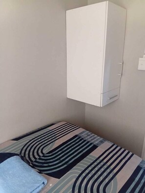 Una habitación pequeña con una cama, un armario blanco y un enchufe.