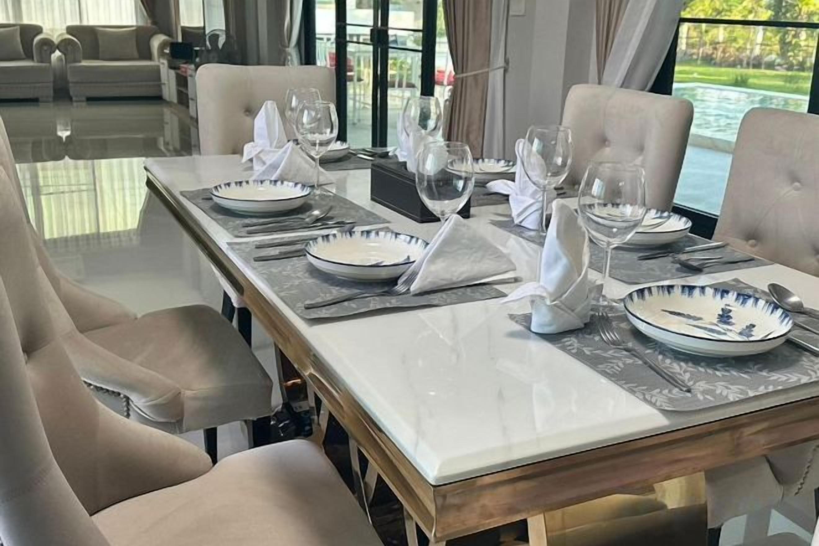 Een eettafel gedekt voor zes personen, met witte borden, bestek en glazen, in een kamer met uitzicht op een waterlichaam.