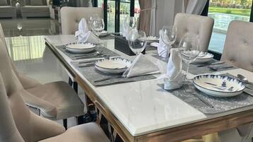 Een eettafel gedekt voor zes personen, met witte borden, bestek en glazen, in een kamer met uitzicht op een waterlichaam.