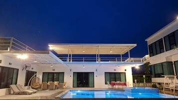 Un espace piscine avec des chaises longues, un coin salon abrité et un bâtiment doté de grandes fenêtres.