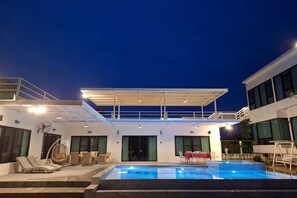 A pool area with lounge chairs, a covered seating area, and a building with large windows. - The Pano Hill (Pak Chong)