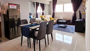 A modern living room with a dining area, a large window with curtains, a sofa, a coffee table, and a TV stand. - KLIA Sepang Alanis Comfort One Bed Room Unit (Sepang)
