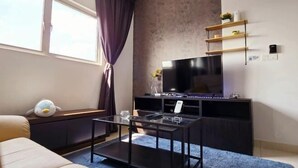 A modern living room with a large flat-screen TV, a glass coffee table, a sofa, and a window with curtains. - KLIA Sepang Alanis Comfort One Bed Room Unit (Sepang)