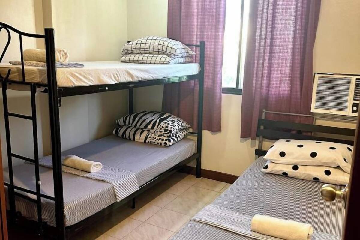 A dormitory room with bunk beds, a window with curtains, and an air conditioning unit.