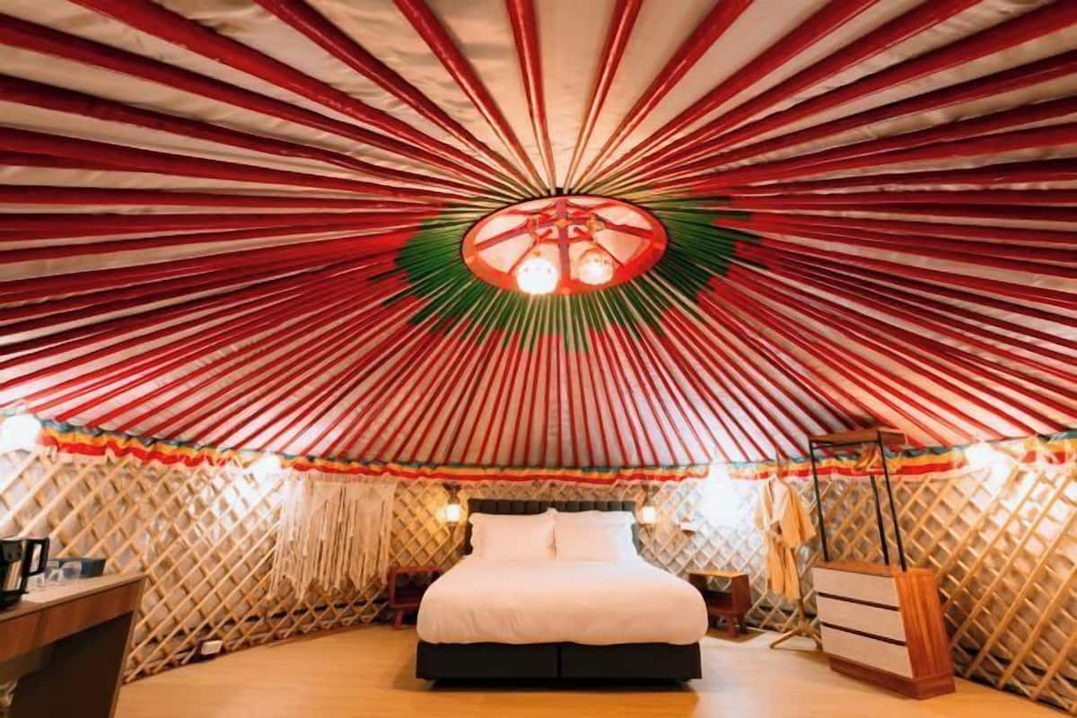 A yurt with a bed, a small table, and a lamp.