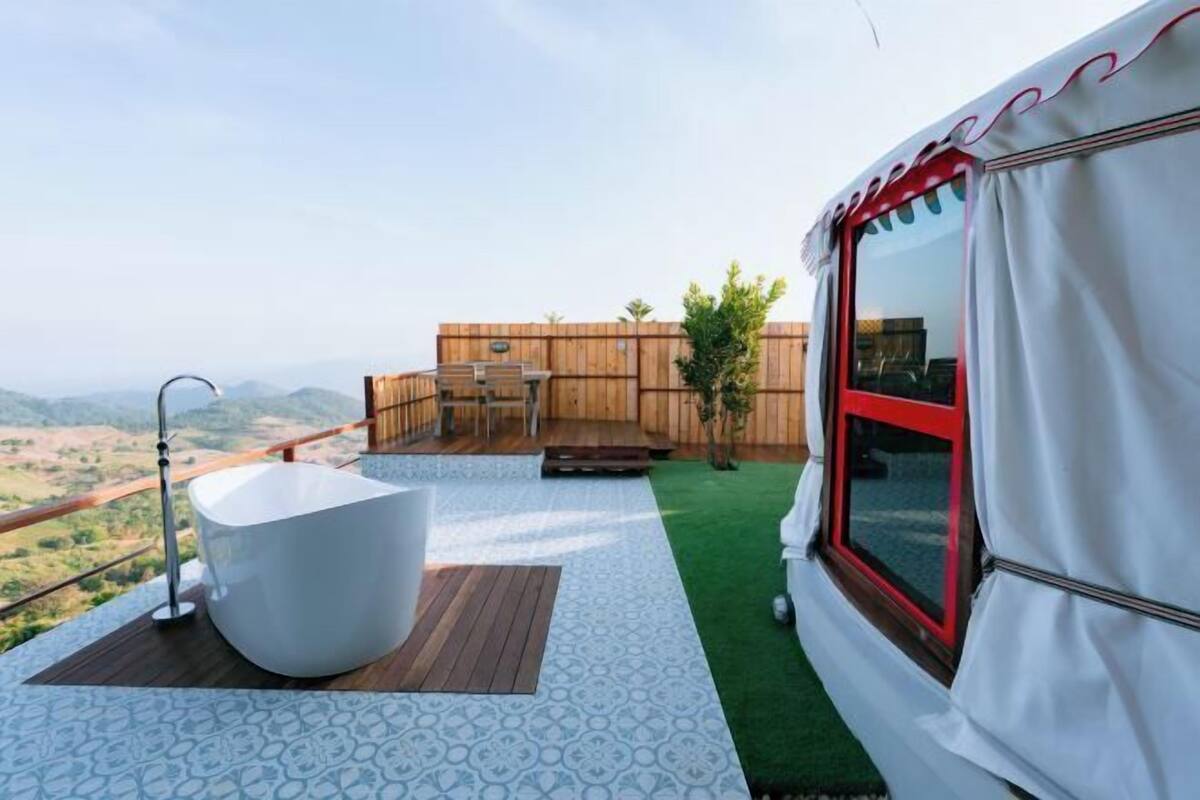 Un balcon avec une baignoire blanche, une terrasse en bois et une vue sur la campagne.