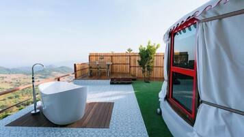 A balcony with a white bathtub, a wooden deck, and a view of the countryside.