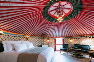 Une yourte comprenant un lit, un coin salon et un luminaire central.