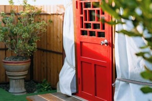 A red door with a white curtain, a wooden fence, and a potted plant in the background. - Oasis Yurt Villa @ Doi Lan (Mae Suai)