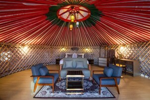 L’intérieur chaleureux d’une yourte, avec un lit au centre, deux canapés, une petite table et un tapis à motifs.